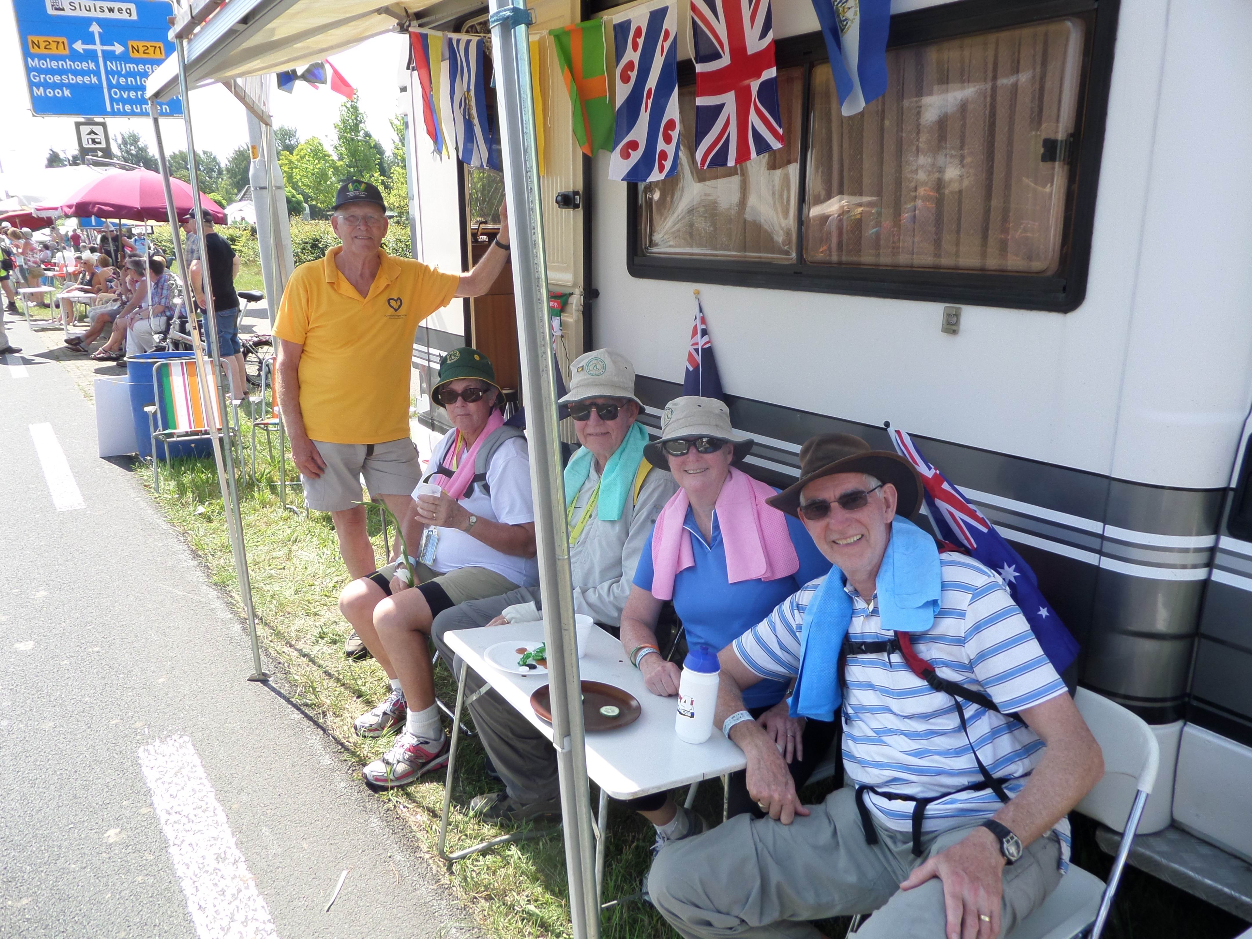 Four adult walkers seated and one man standing in front of a caravan.